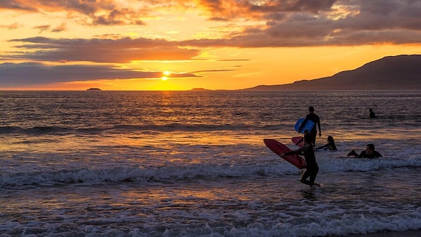 Een zonsondergang boven de oceaan, met een persoon die een surfplank draagt.