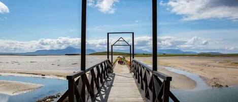 A wooden bridge with a metal railing leading to a structure with a triangular roof.