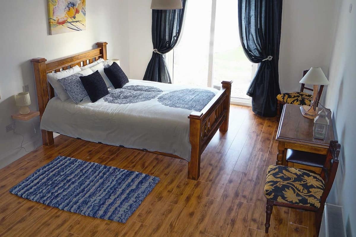 Une chambre à coucher avec un lit en bois, un tapis bleu à motifs, une table de chevet avec une lampe et une chaise avec un coussin à motifs.