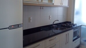 A modern kitchen with white cabinets, a black countertop, a built-in oven, and a refrigerator. - BEAUTIFUL AND COMFORTABLE 3QTS APARTMENT ON THE BEACH OF ENGLISH IN 180 MTS FROM THE BEACH (Ingleses do Rio Vermelho)