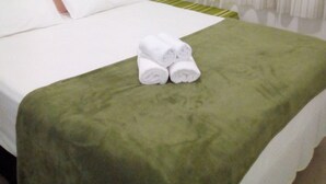 A hotel room with a bed, green bedspread, white pillows, and a pair of rolled towels on the bed. - BEAUTIFUL AND COMFORTABLE 3QTS APARTMENT ON THE BEACH OF ENGLISH IN 180 MTS FROM THE BEACH (Ingleses do Rio Vermelho)