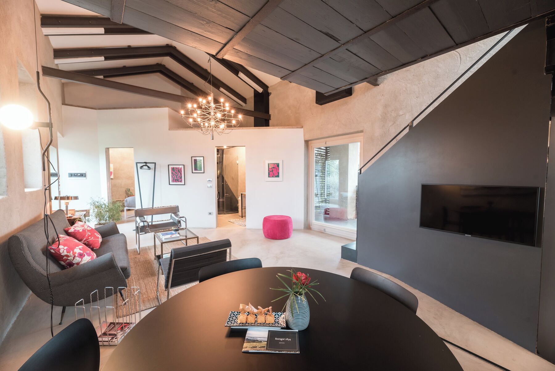 Ein modernes Wohnzimmer mit dunkler Wand, einem runden Tisch mit einer Vase und einer Couch mit roten Kissen.