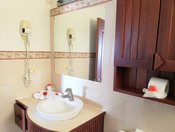 A bathroom with a sink, mirror, hairdryer, and wooden cabinet. - KiteBeach Agualina Oceanfront Condo Complex in Hotel (Cabarete)