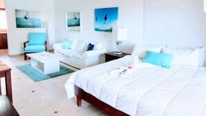 A hotel room with a bed, a white sofa, a blue armchair, and a small table. - KiteBeach Agualina Oceanfront Condo Complex in Hotel (Cabarete)