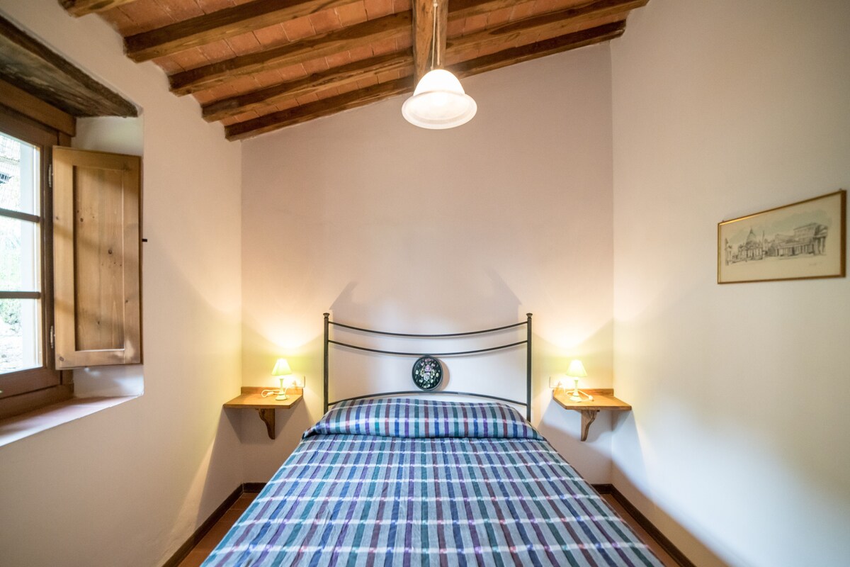 A bedroom with a bed, two bedside lamps, a window, and a wooden ceiling.
