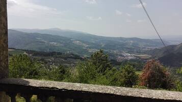 Vista panorámica desde un balcón con barandilla de piedra que domina un valle con montañas al fondo.
