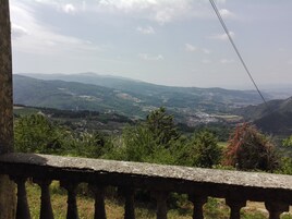 Vista panorámica desde un balcón con barandilla de piedra que domina un valle con montañas al fondo.