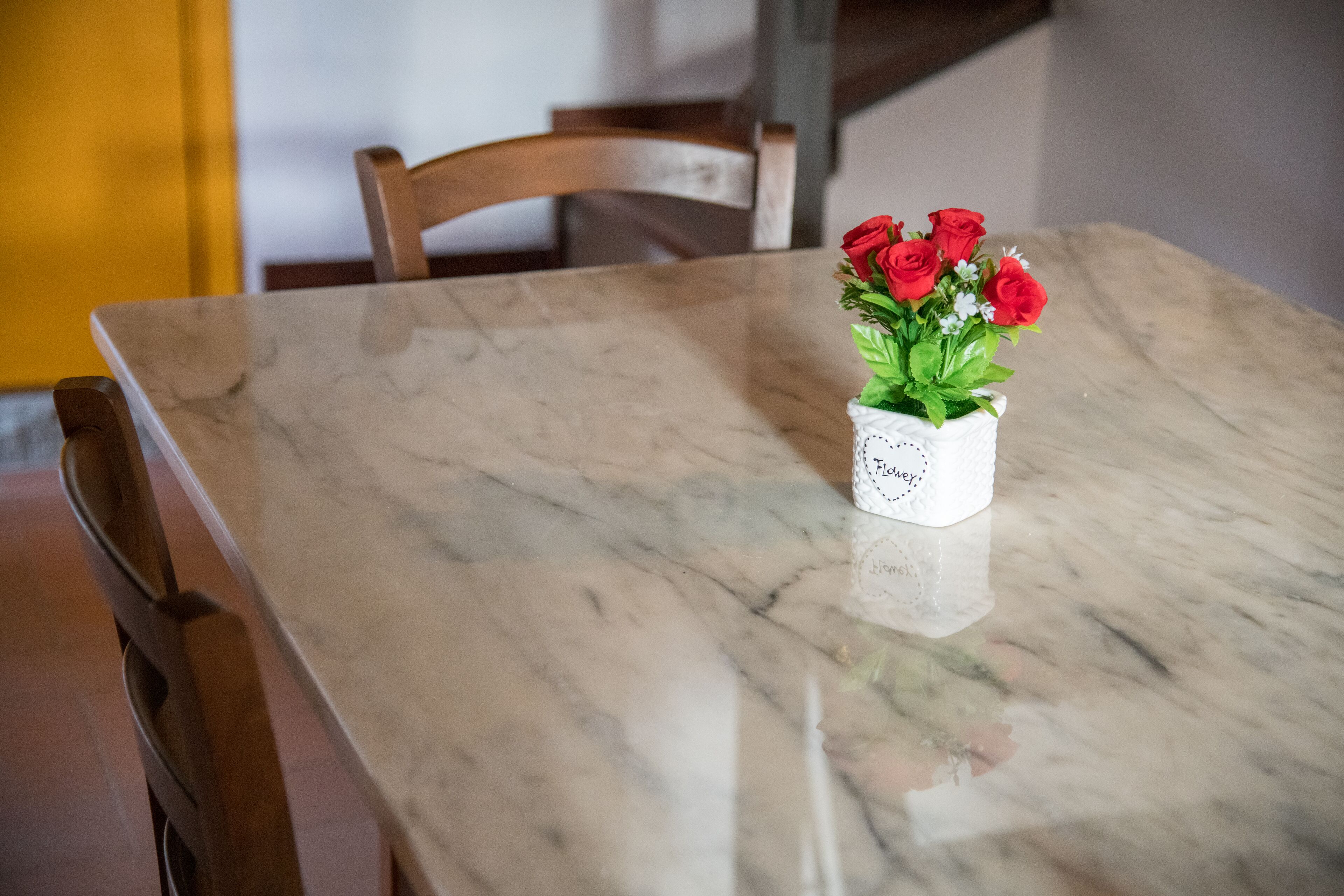Una mesa de mármol con un jarrón blanco que contiene rosas rojas.