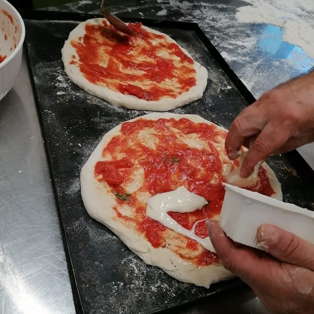 A person preparing pizza dough with tomato sauce and cheese on a baking tray.