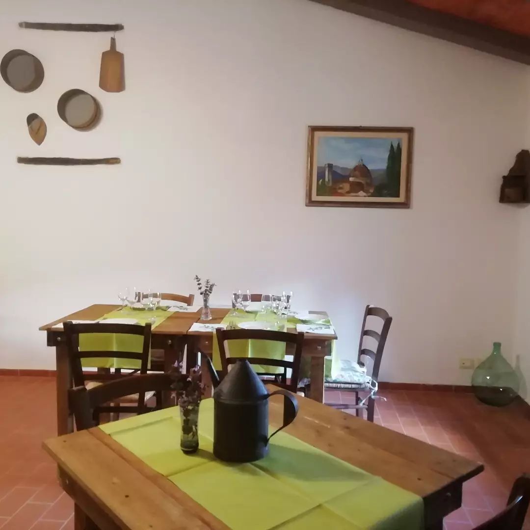 Ein Essbereich mit einem Holztisch, Stühlen und einer grünen Tischdecke. Auf dem Tisch steht eine Vase mit Blumen und eine schwarze Karaffe.