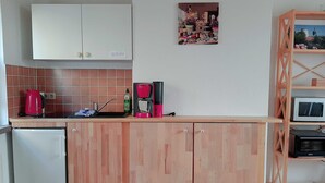 A compact kitchen with wooden cabinets, a refrigerator, a sink, and a coffee maker. - Vacation apartment at the Stadtpark_Seerose - Holiday apartments at the Stadtpark (Lutherstadt Wittenberg)