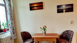 A room with a wooden table, two floral-patterned chairs, a vase with flowers, and two wall-mounted paintings. - Vacation apartment at the Stadtpark_Seerose - Holiday apartments at the Stadtpark (Lutherstadt Wittenberg)
