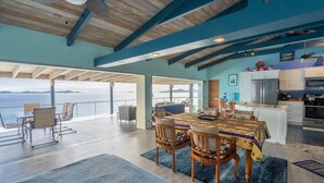 Une salle à manger spacieuse avec vue sur la mer, des poutres apparentes en bois au plafond et une cuisine moderne.