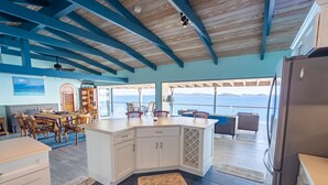 Une cuisine spacieuse dotée d’un grand îlot central, de poutres apparentes en bois et offrant une vue sur la mer.