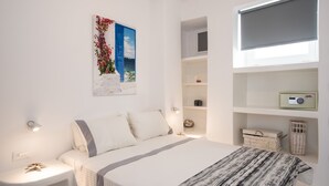 Quarto com cama, mesas de cabeceira, prateleira na parede e janela com cortina.