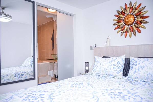 A bedroom with a large bed, a mirror, a sunburst wall decoration, and a shower area.