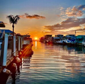 A marina with boats docked, a wooden pier, and a sunset in the background. - Happy Place Key Largo - Waterfront Vintage Coastal Cottage (Key Largo)