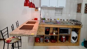 A compact kitchen with white cabinets, a granite countertop, and a red pendant light.
