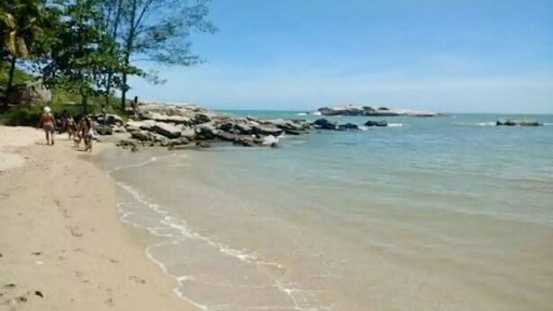 A beach with clear water, rocky outcrops, and people walking along the shore.