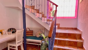 A staircase with a handrail, a bench with cushions, a chair, a potted plant, and a small table with framed photos and a decorative item. - Villa Coyoacan (Mexico City)
