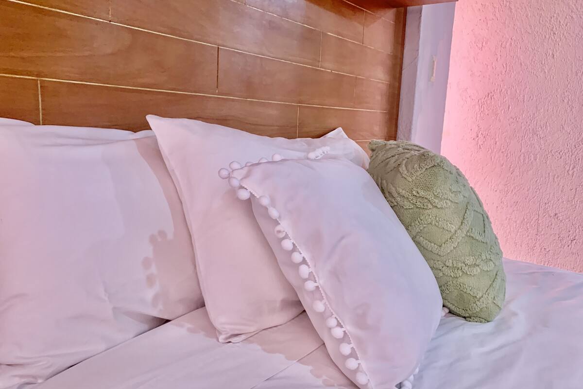 Een bed met witte beddengoed en meerdere kussens, waaronder een groen kussen met structuur.