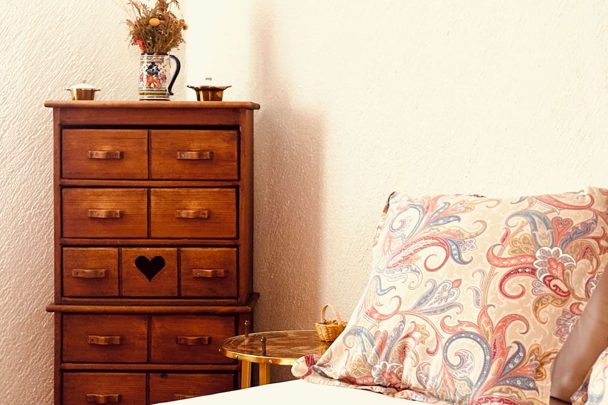 Een houten dressoir met meerdere lades, een klein rond tafeltje en een bed met een gestreept kussen.