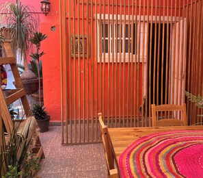 A red-walled room with a wooden gate, a window, and a table with a colorful rug.