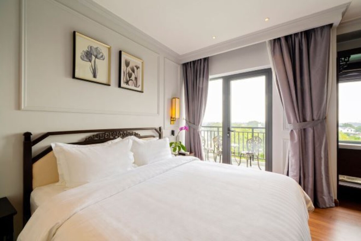 Un dormitorio con una cama grande, un balcón con vistas y dos cuadros con motivos florales en la pared.