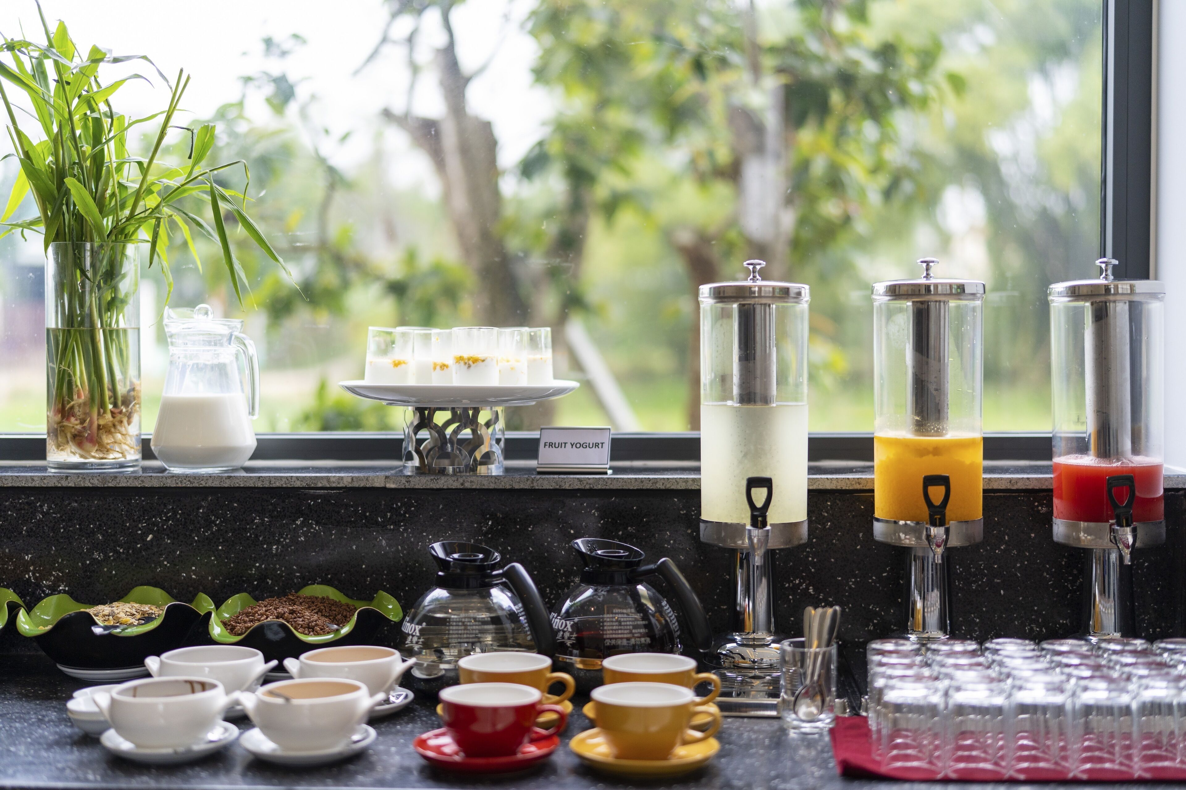 Un bar à petit-déjeuner proposant du café et du thé, un distributeur de yaourts aux fruits et une vue sur la verdure environnante.