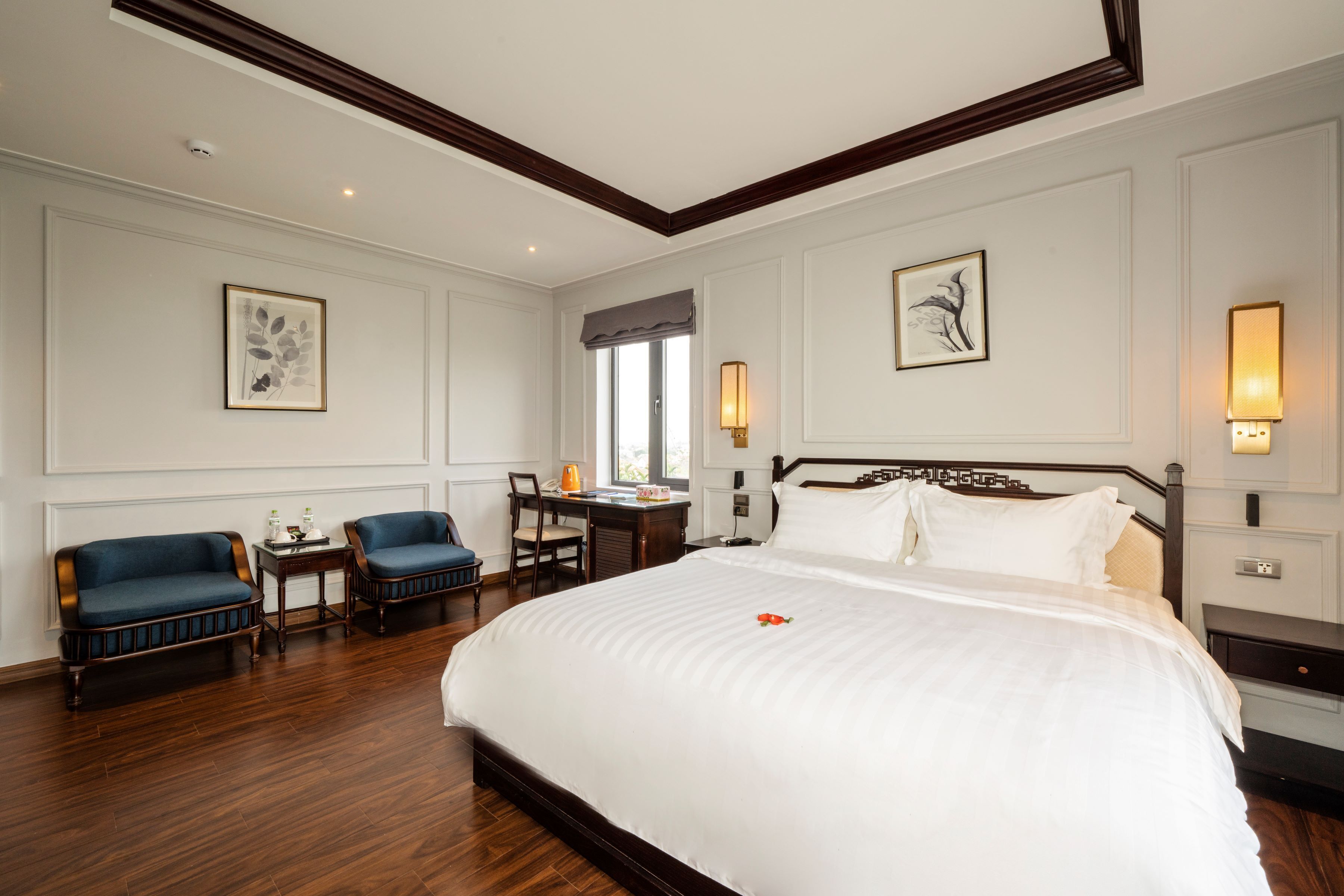 A hotel room with a large bed, two armchairs, a desk, and a window with a view.