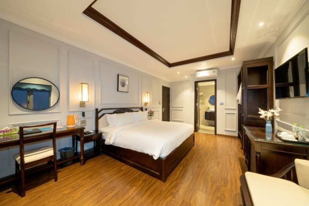 Habitación de hotel con una cama de madera, un escritorio con una silla, un espejo redondo y una mesita de noche con una lámpara.