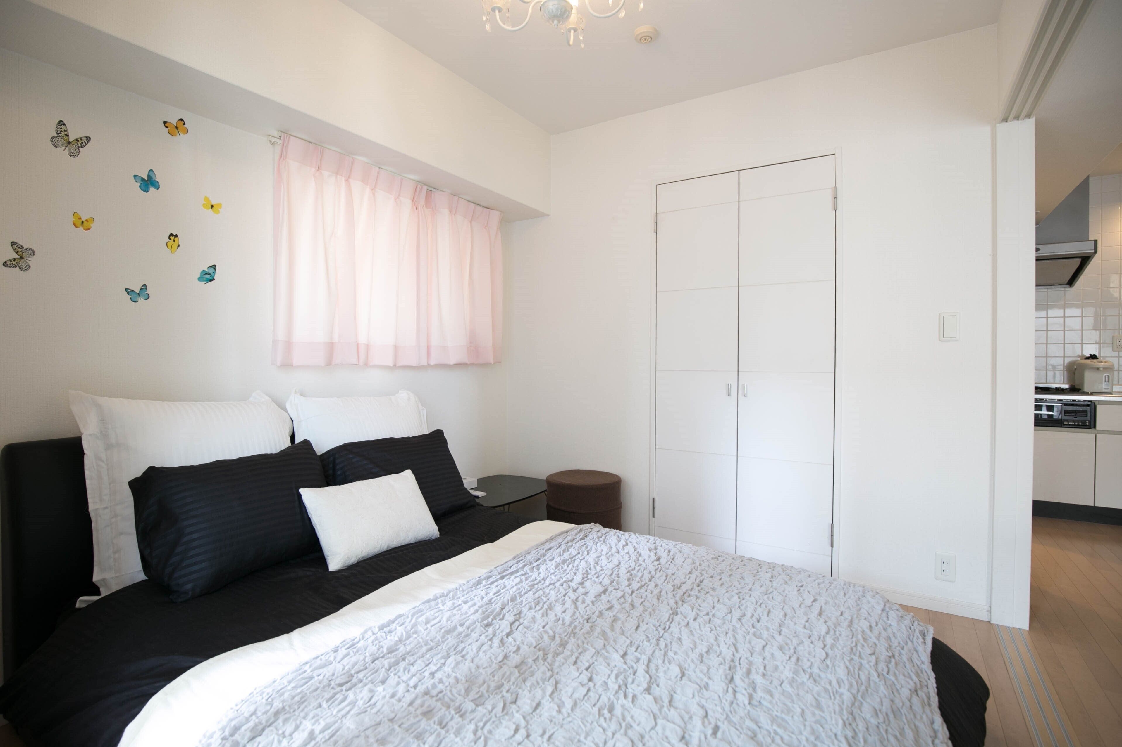 A bedroom with a bed, pillows, a nightstand, a small round table, a wardrobe, and a window with curtains.