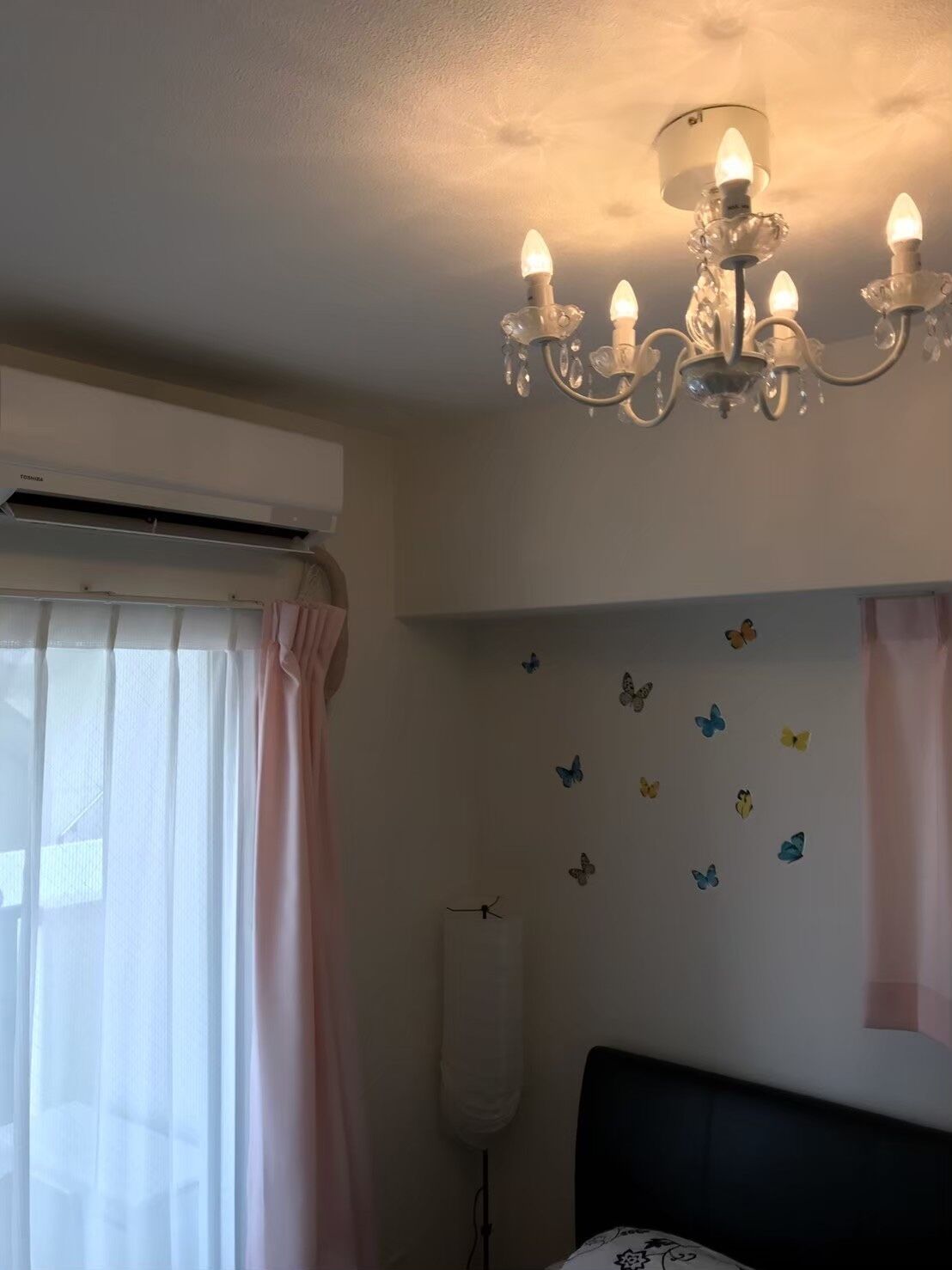 Une chambre à coucher avec un lustre, un climatiseur, des rideaux et des autocollants décoratifs représentant des papillons sur les murs.