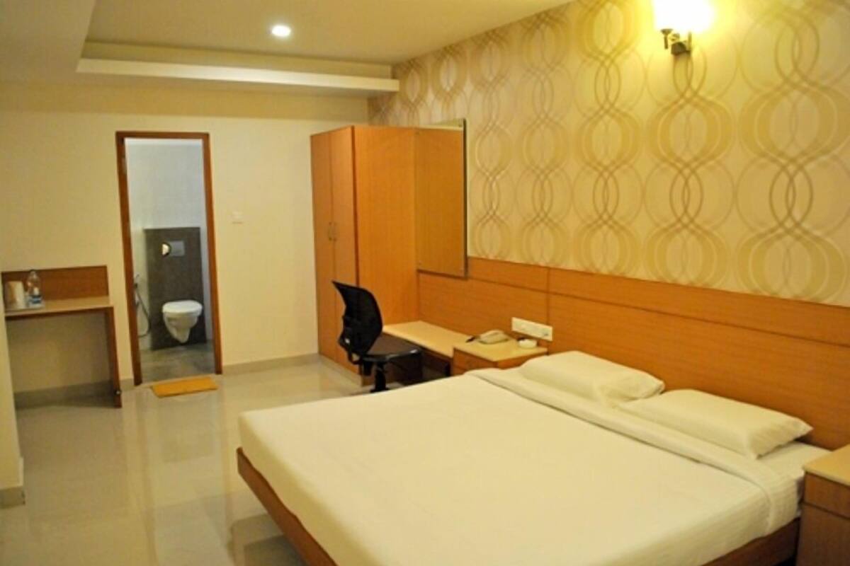 A hotel room with a bed, a desk, a chair, a wardrobe, and a bathroom visible through an open door.