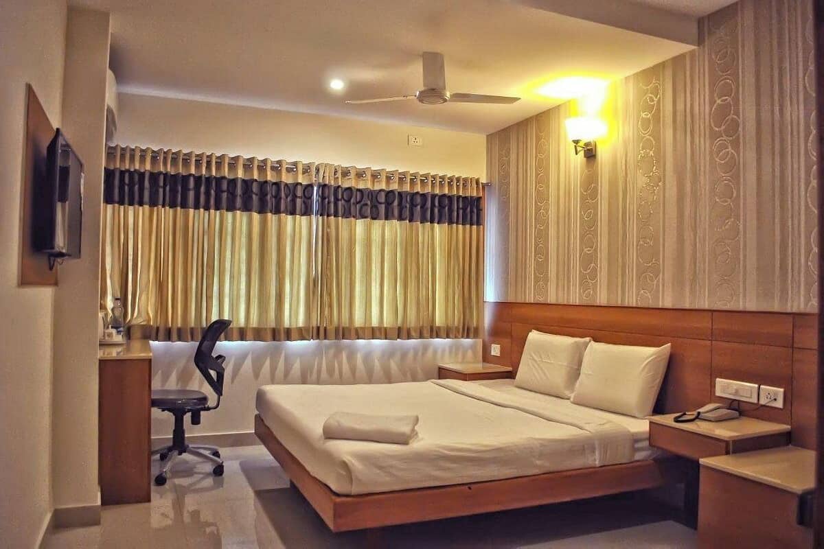 A hotel room with a large bed, a desk with a chair, a ceiling fan, and a window with curtains.