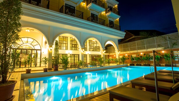 A swimming pool with lounge chairs, potted plants, and a building with balconies and arched windows. - Angkor Zhe Jiang Hotel (Siem Reap)