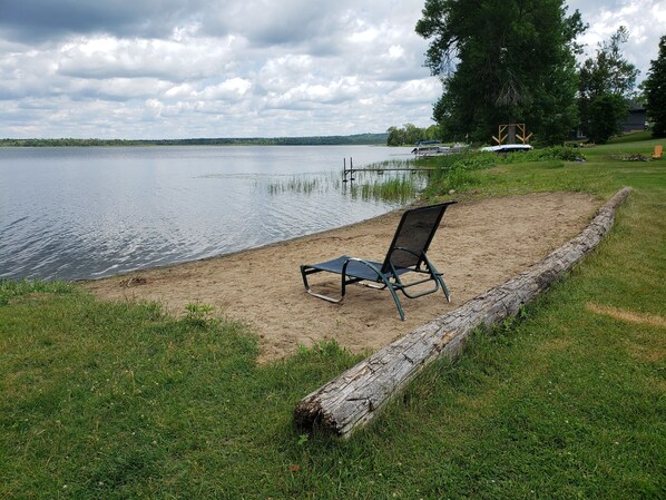 A beach with a single metal chair and a wooden log barrier.