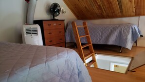Une chambre avec une échelle en bois, un lit recouvert d’une courtepointe matelassée, une commode et un climatiseur blanc.