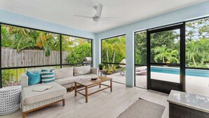 Ein modernes Wohnzimmer mit einer Couch, einem Couchtisch und großen Fenstern mit Blick auf einen Pool.