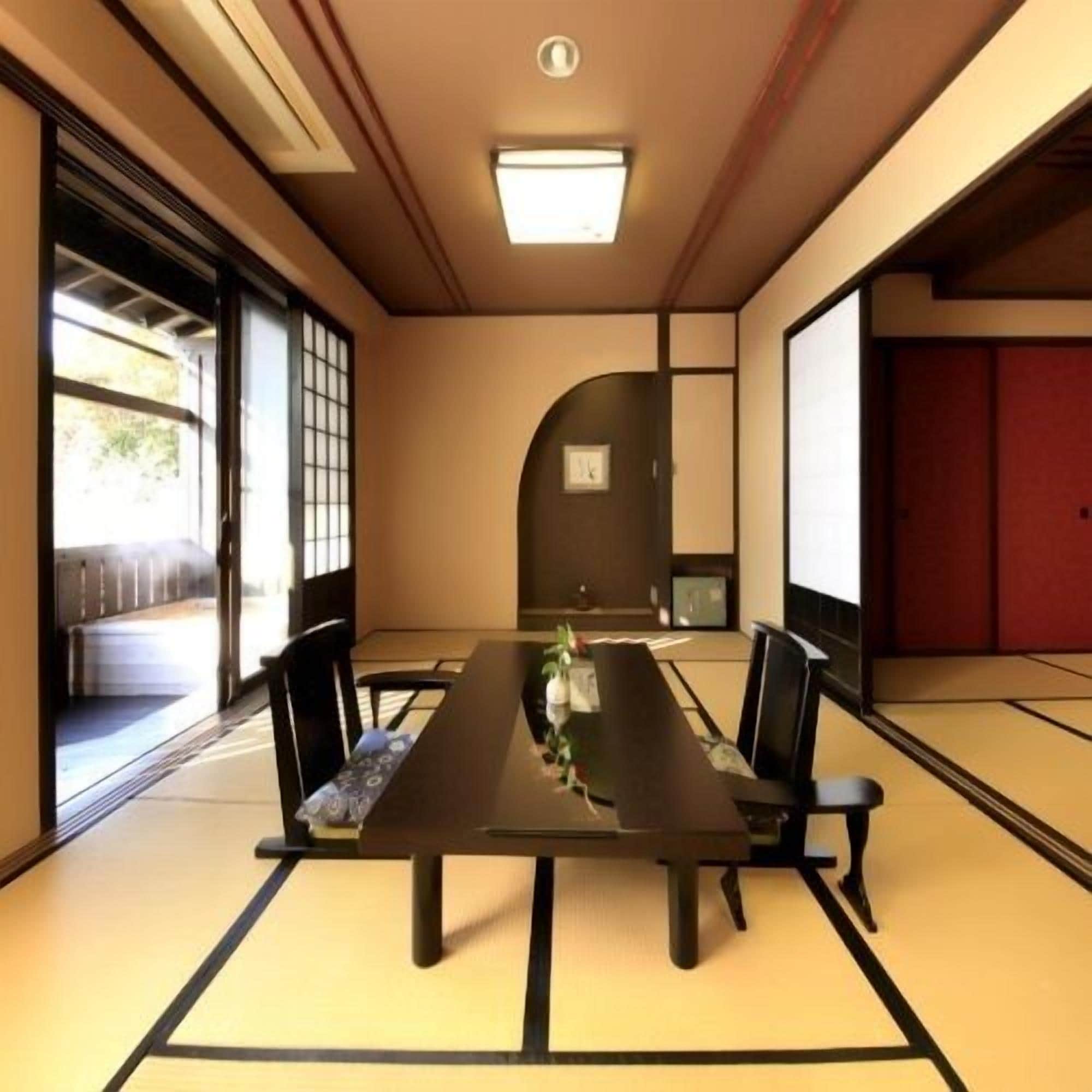 A traditional Japanese meeting room with tatami flooring, a low table, and black chairs.