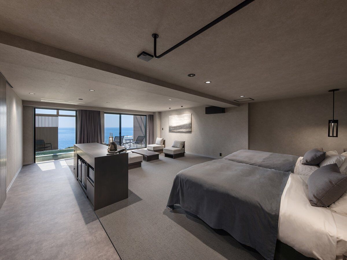 Ein modernes Hotelzimmer mit einem großen Bett, einem Schreibtisch und einer Sitzecke mit Meerblick.