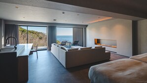 A modern hotel room with a large bed, a sofa, a dining area, and a fireplace. - TheMana Village (Tosashimizu)