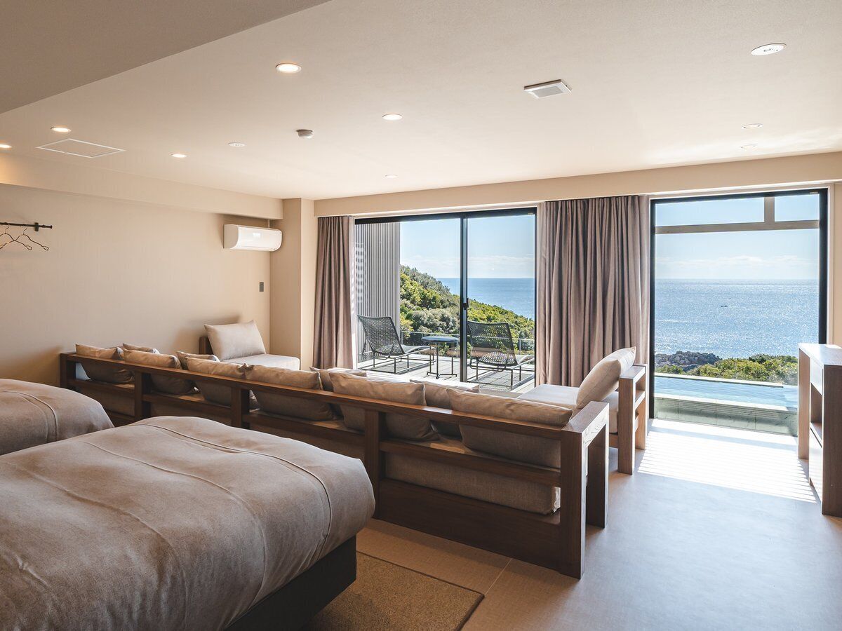 A modern hotel room with a large bed, a sofa, a dining table, and a view of the ocean.