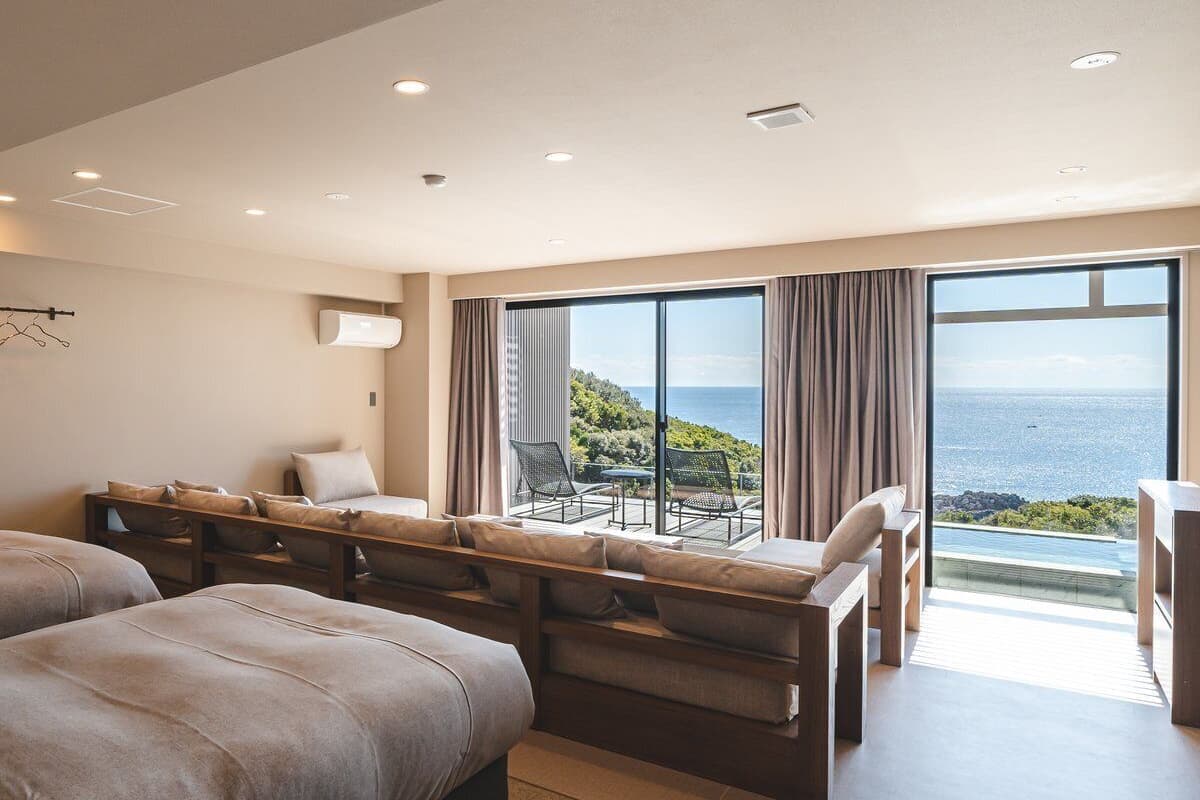 Ein modernes Hotelzimmer mit einem großen Bett, einer Couch, einem Esstisch und Blick auf den Ozean.