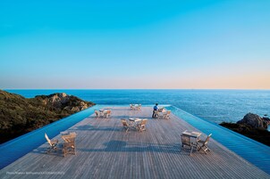 Una piscina infinita con terraza de madera y sillones de descanso con vistas al océano.