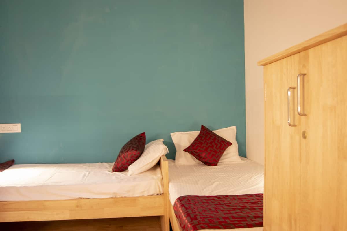 Two single beds with red and white bedding, a wooden wardrobe, and a teal wall.