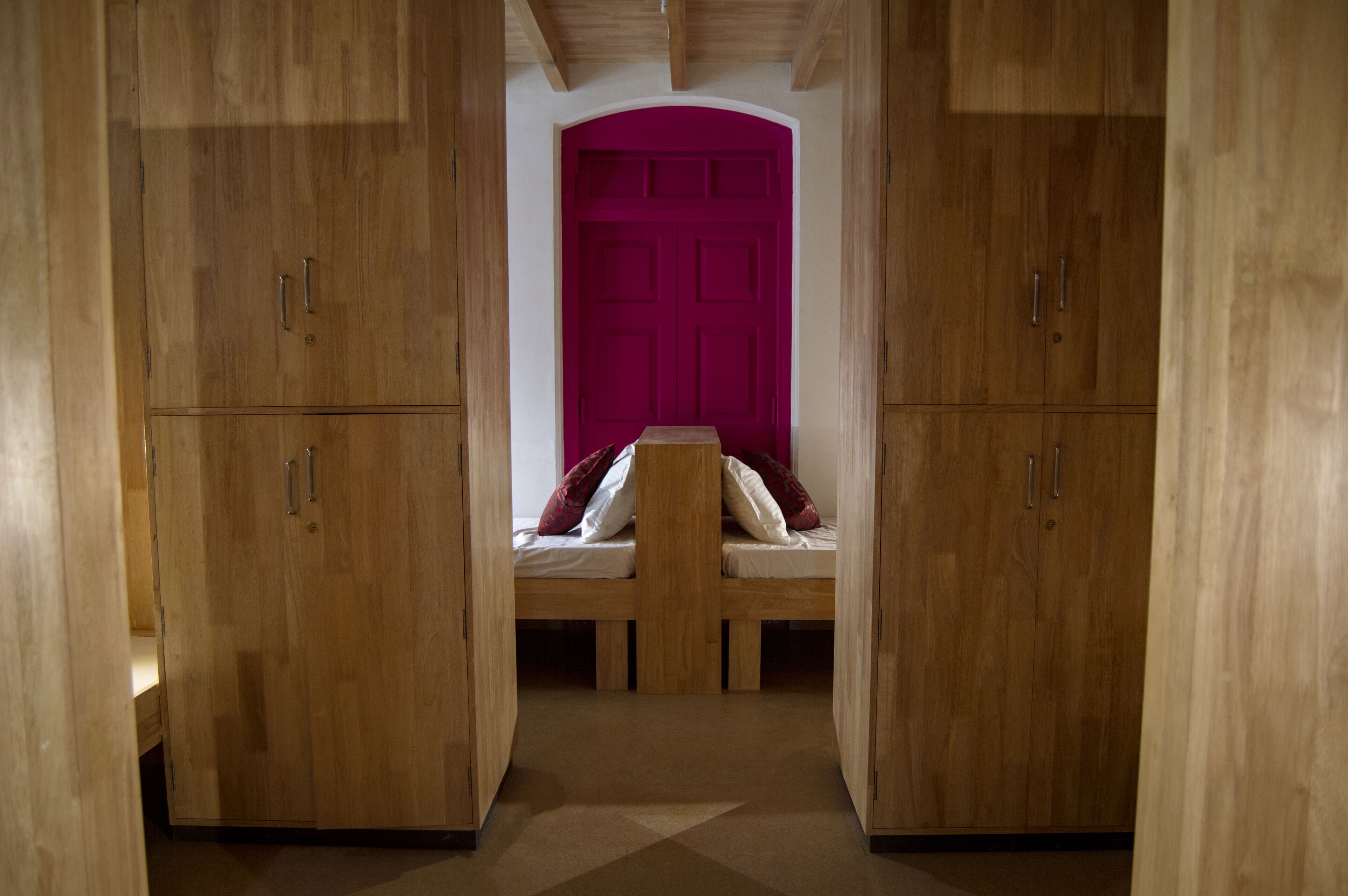 A room with wooden cabinets, a bed with pillows, and a bright pink door.