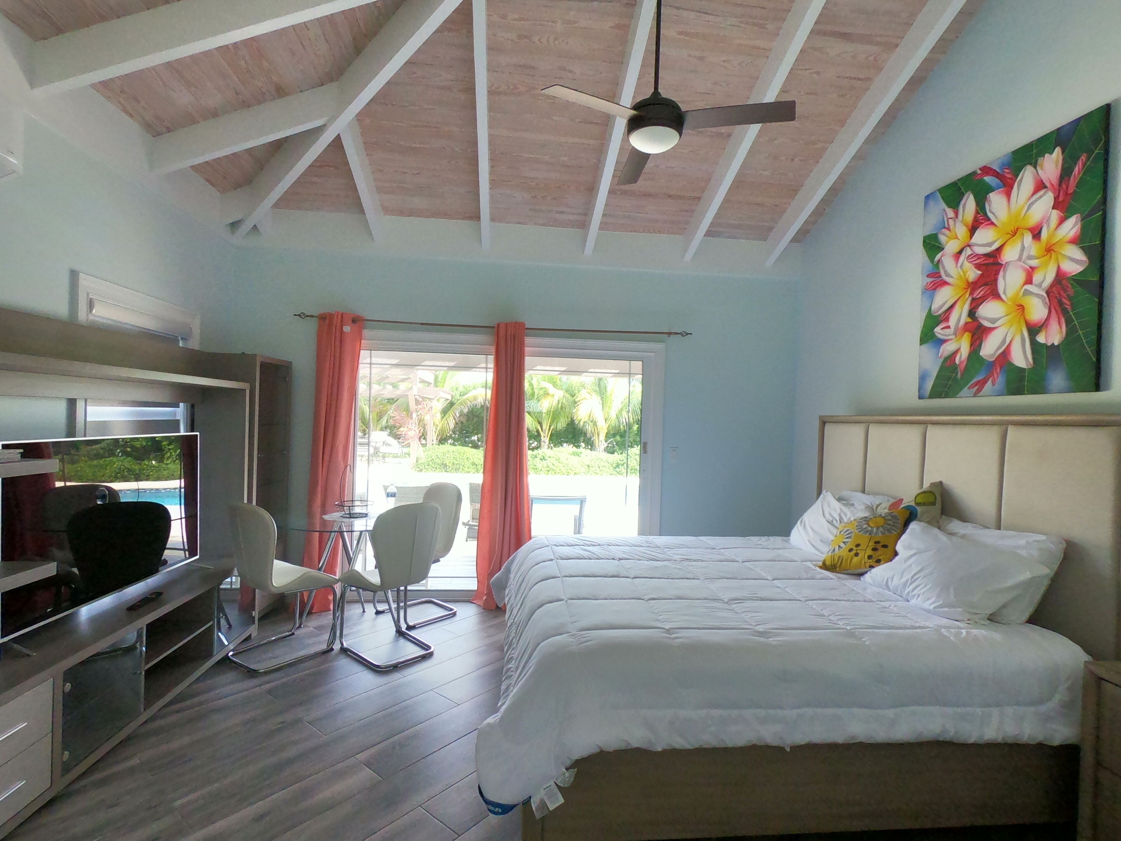 A bedroom with a bed, a desk, a chair, a ceiling fan, and a painting.