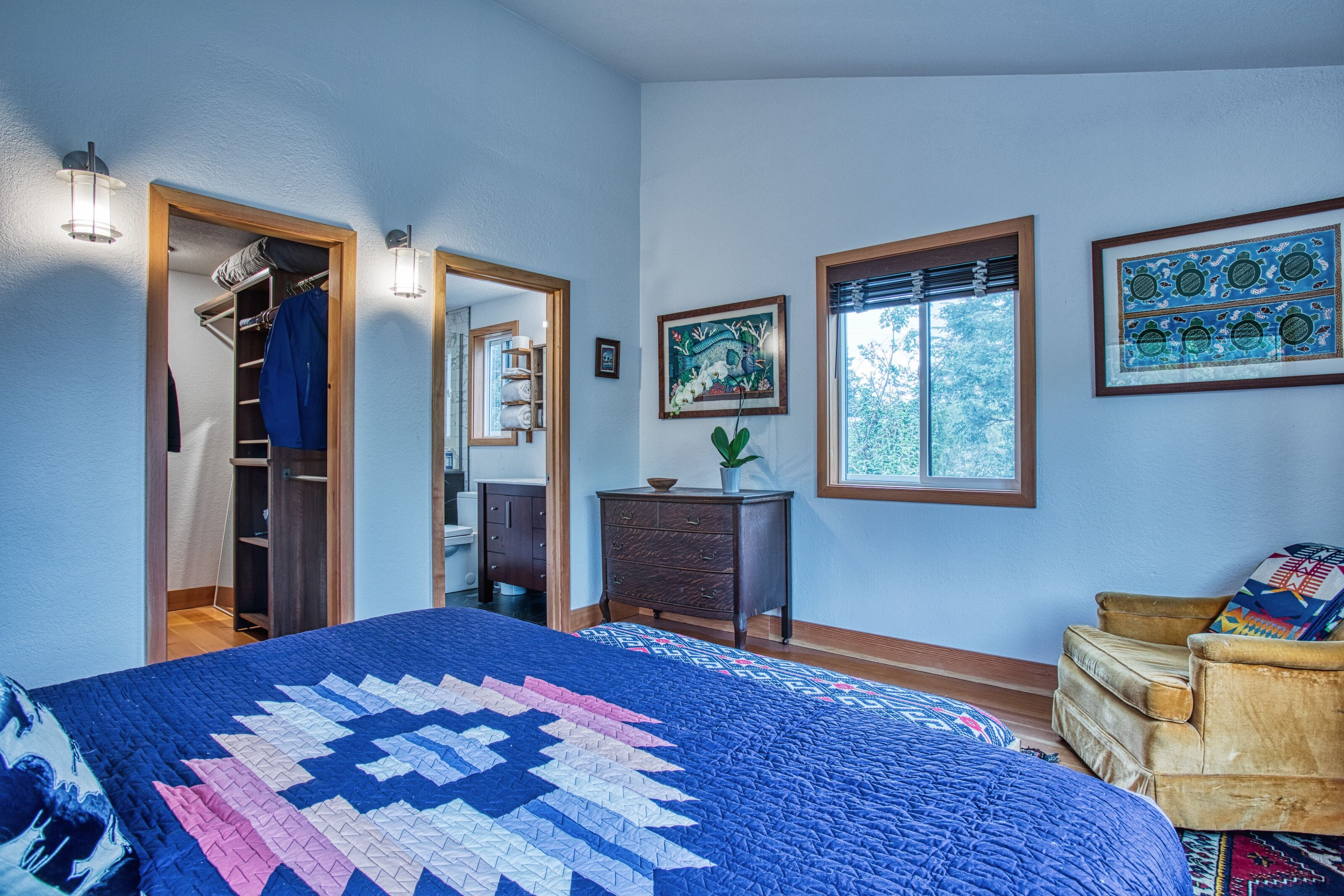 Un dormitorio con una cama grande, un armario, una cómoda y una silla. Hay dos ventanas y una puerta que da a un armario.