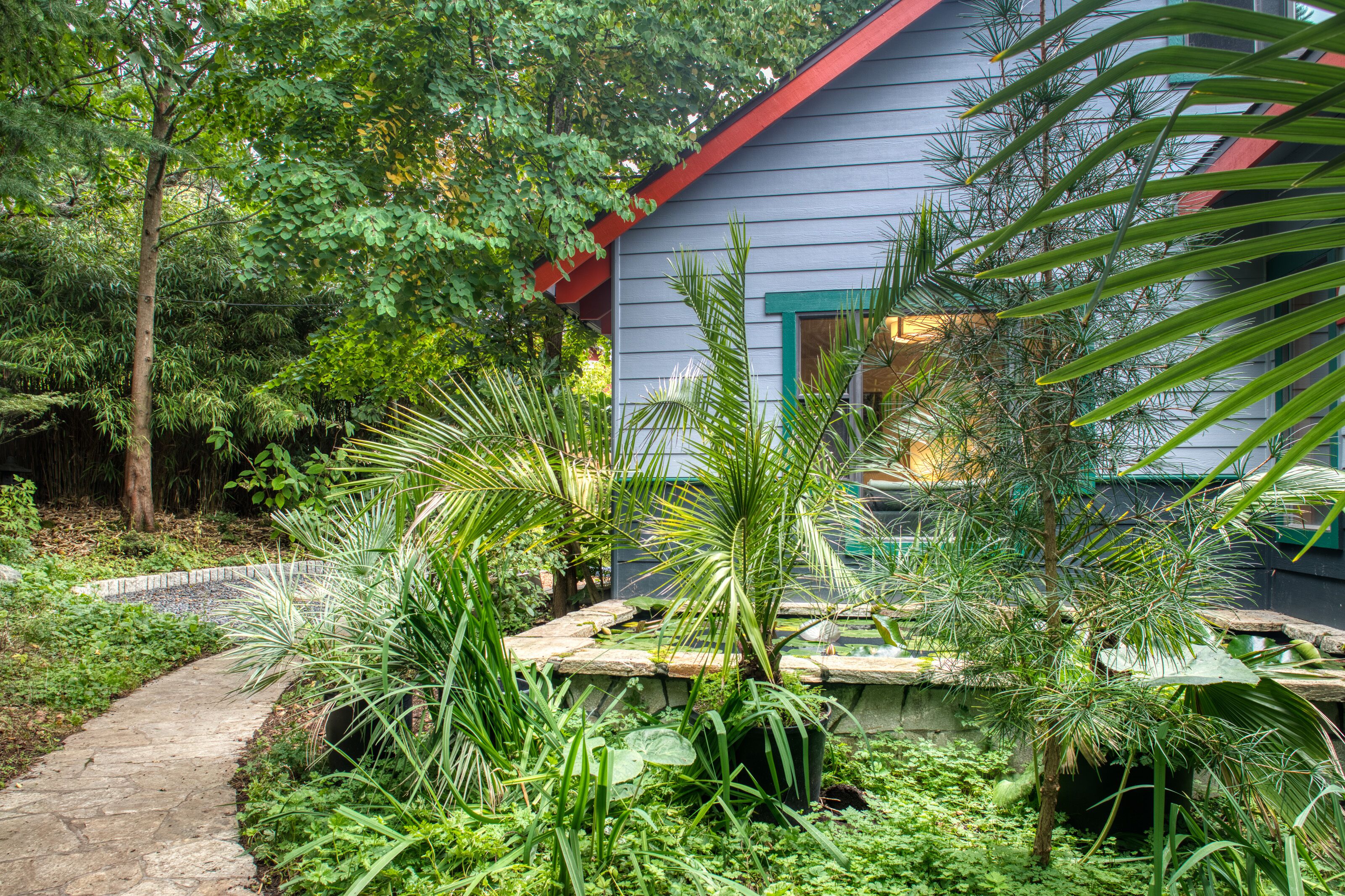 A house with a red roof and a garden with various plants and a stone pathway.